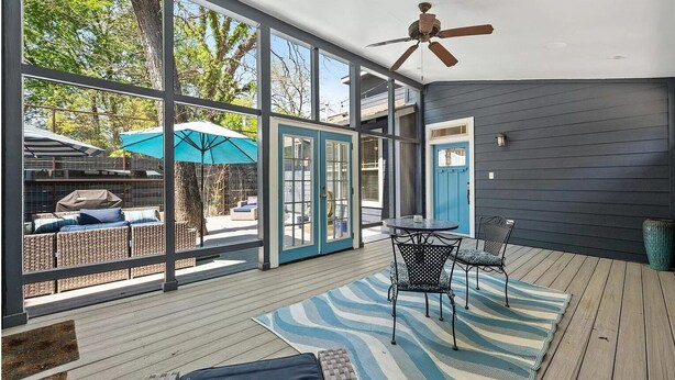 Une terrasse couverte avec un ventilateur de plafond, une table avec des chaises et une vue sur le jardin arrière.