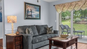 A living room with a gray sofa, a wooden side table, a coffee table, and a large window with a view of the outdoors. - Uniquely charming Pet Friendly 2 Bed condo near the strip at Pointe Royale! (Branson)