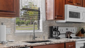 A kitchen with wooden cabinets, a white microwave, a coffee maker, and a window with blinds. - Uniquely charming Pet Friendly 2 Bed condo near the strip at Pointe Royale! (Branson)