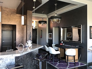 Uma cozinha moderna com bancada de mármore, área de bar embutida, banquetas brancas e um espelho grande acima do bar.