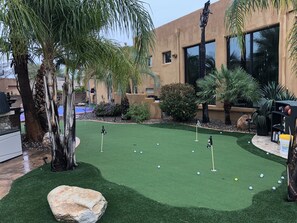 Um campo de mini golfe com grama sintética, buracos marcados por postes e bolas de golfe espalhadas.