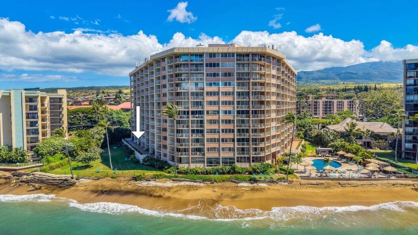 A multi-story hotel with a curved facade, located near a beach with a pool and lounge area.