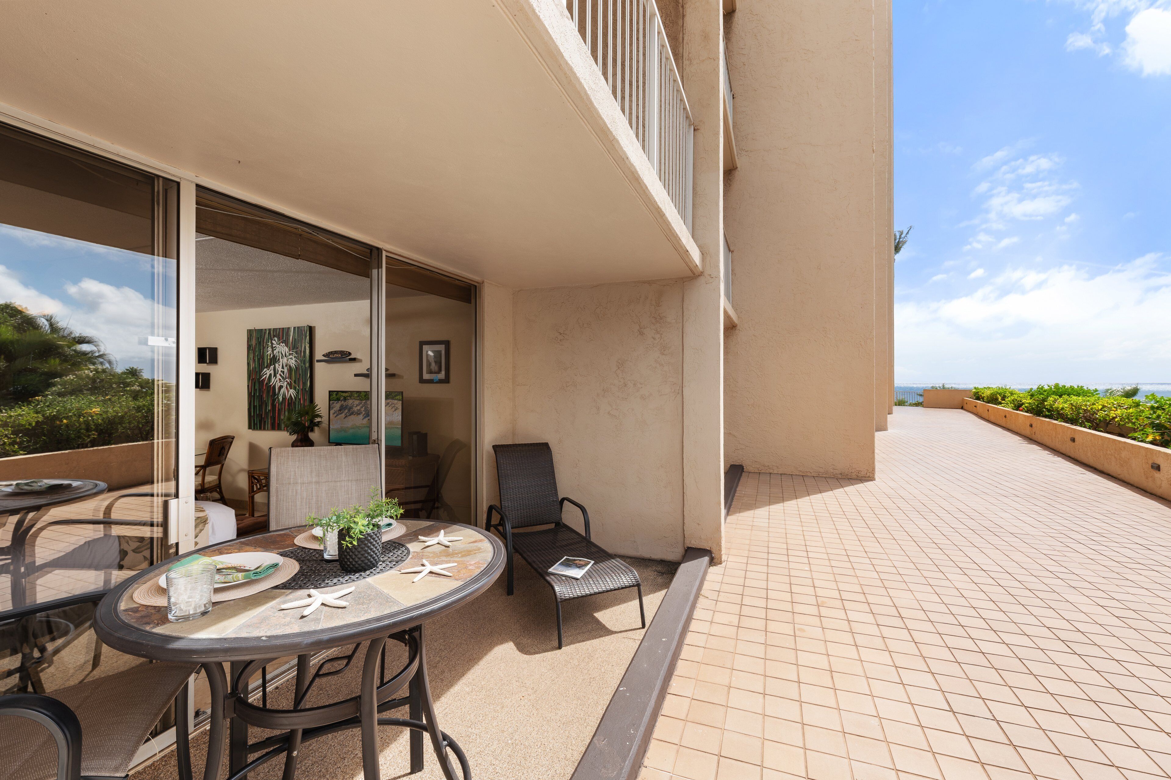 A balcony with a table and chairs, a glass door leading to an indoor area, and a view of the sea.