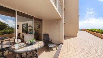 A balcony with a table and chairs, a glass door leading to an indoor area, and a view of the sea.