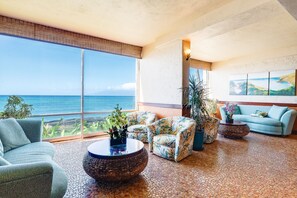 Un salón amplio con un ventanal grande con vistas al océano, amueblado con un sofá, sillones y una mesa de centro.