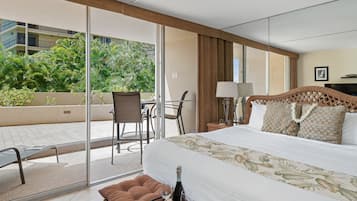 A hotel room with a bed, a small table with a bottle of wine, a chair, and a view of a balcony with plants.
