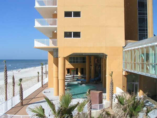 Un hotel de varios pisos con zona de piscina, balcones y vista al mar.