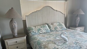 Ein Schlafzimmer mit einem Bett, zwei Nachttischen, einer Lampe auf jedem Nachttisch und einem schwanenförmigen Kopfkissen auf dem Bett.
