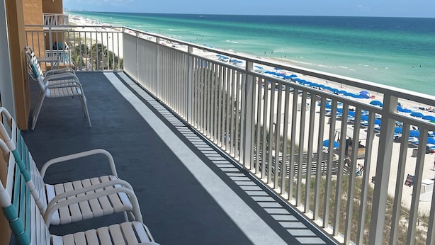 Ein Balkon mit weißen Stühlen und Blick auf einen Strand.
