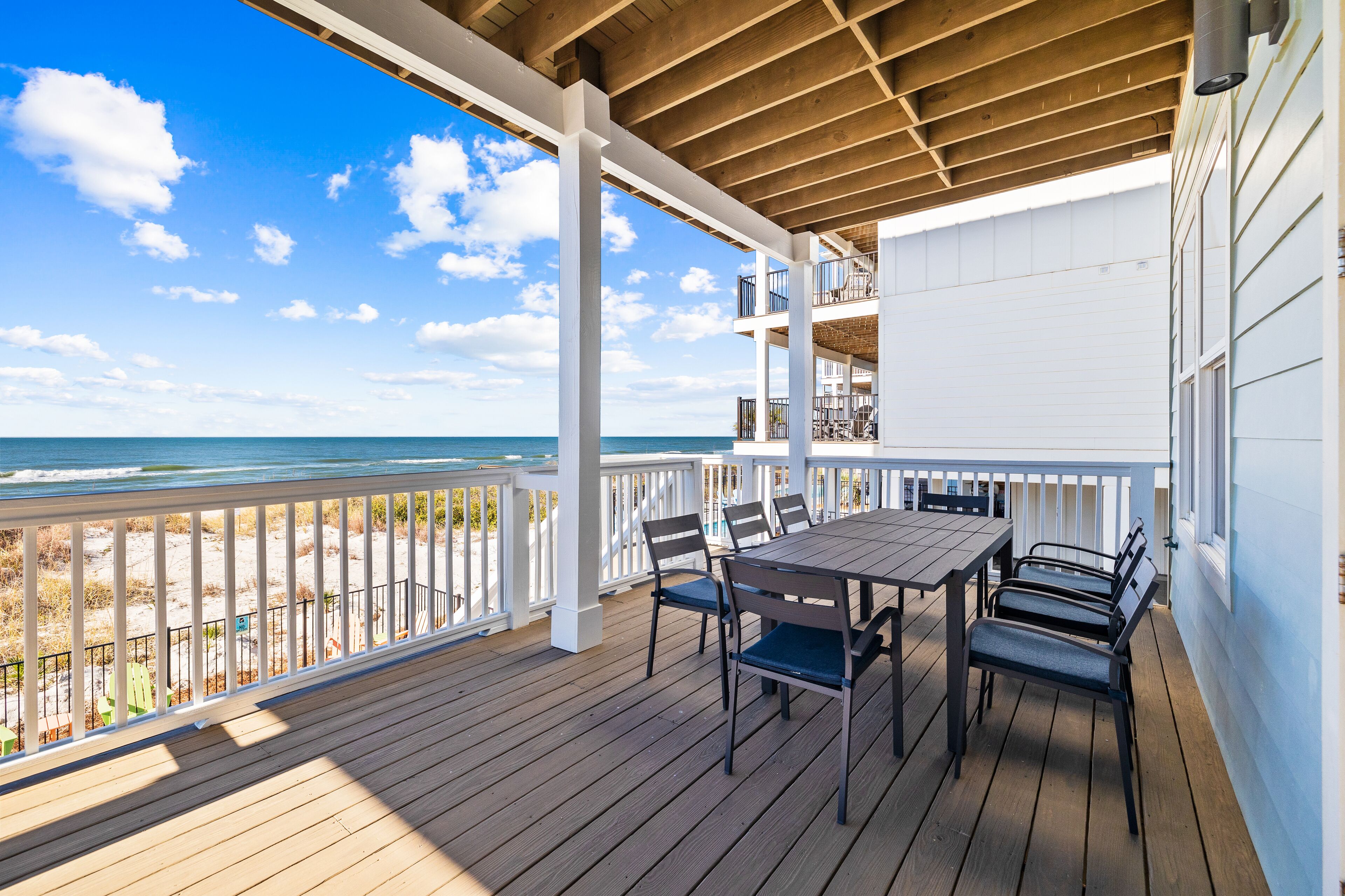A wooden deck with a table and chairs, overlooking a beach.