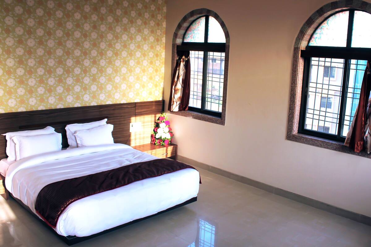 A hotel room with a large bed, two windows, and a floral wall pattern.