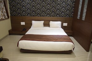 A neatly made bed with a brown headboard, white bedding, and a patterned wallpaper in the background.