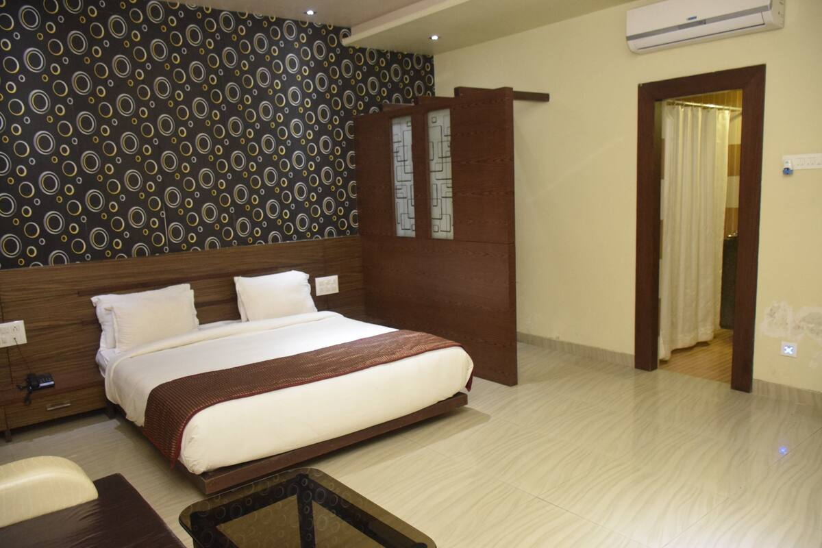 A hotel room with a large bed, a wooden headboard, a patterned wall, and a door leading to another room.