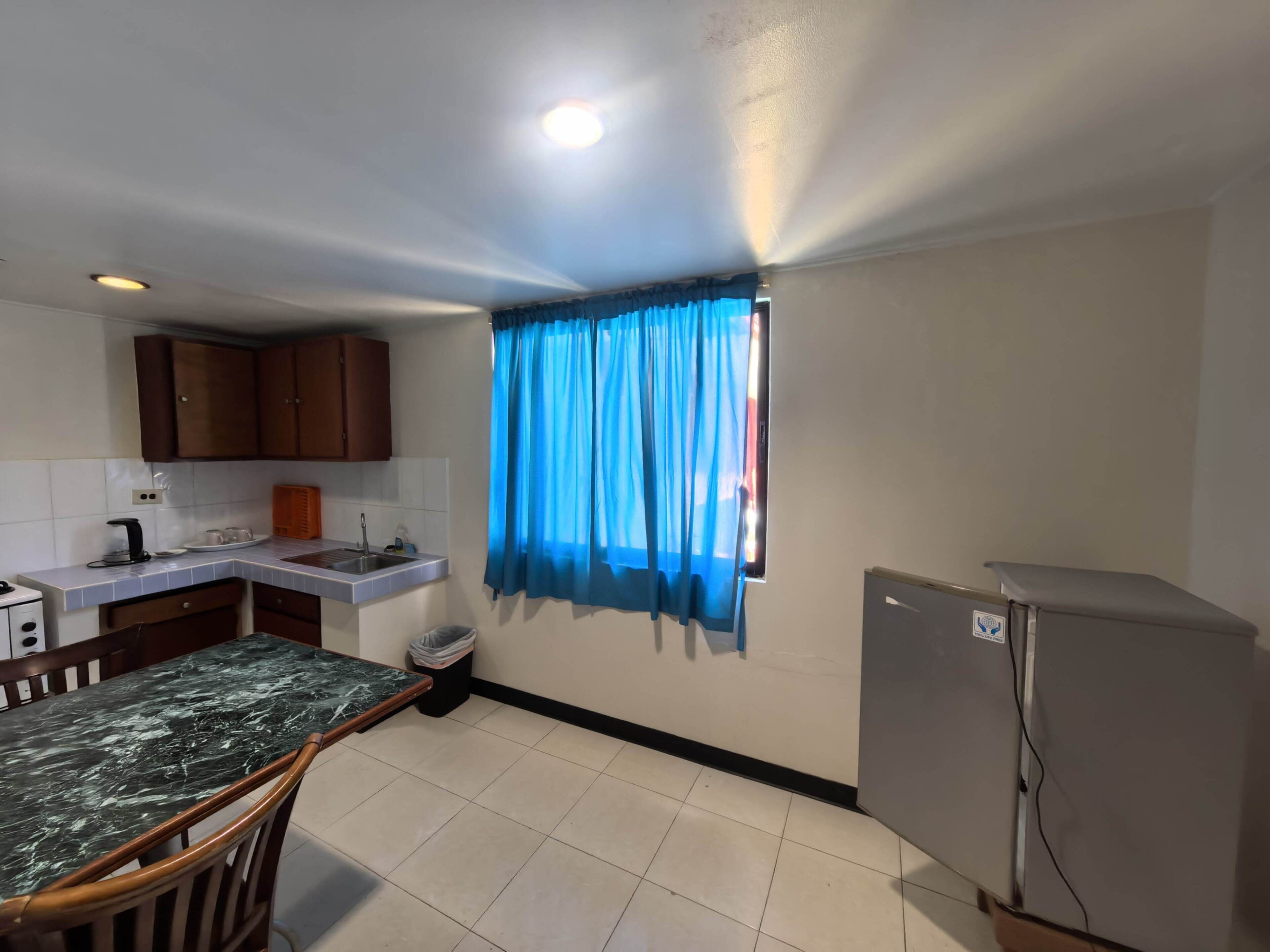A compact kitchen with a sink, cabinets, a refrigerator, and a dining area with a table and chairs.
