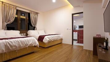 A hotel room with two beds, wooden flooring, a TV, and a minibar.