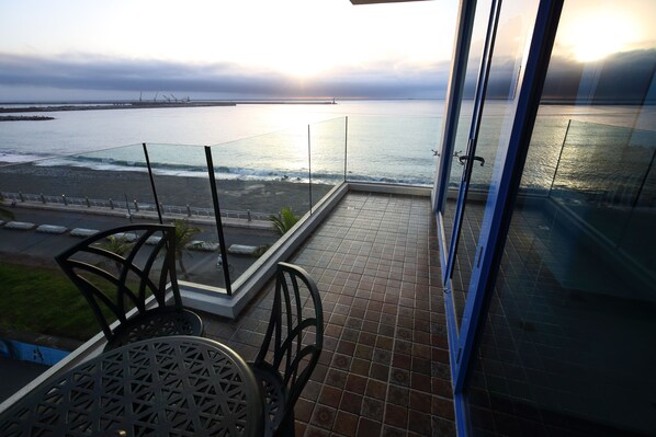A balcony with a view of the sea, a glass railing, and a tiled floor.