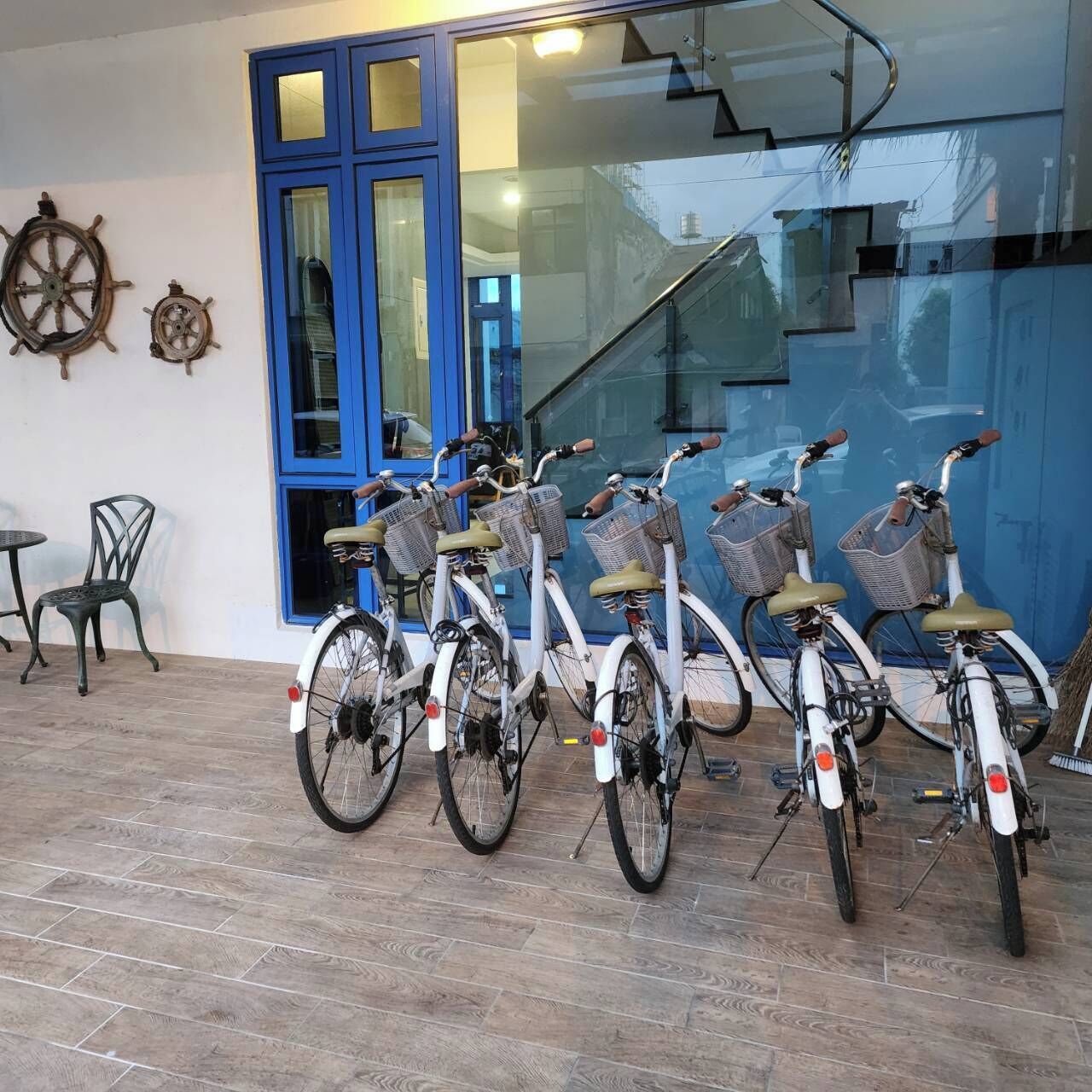A row of bicycles parked outside a building with a blue door and windows reflecting the surroundings.
