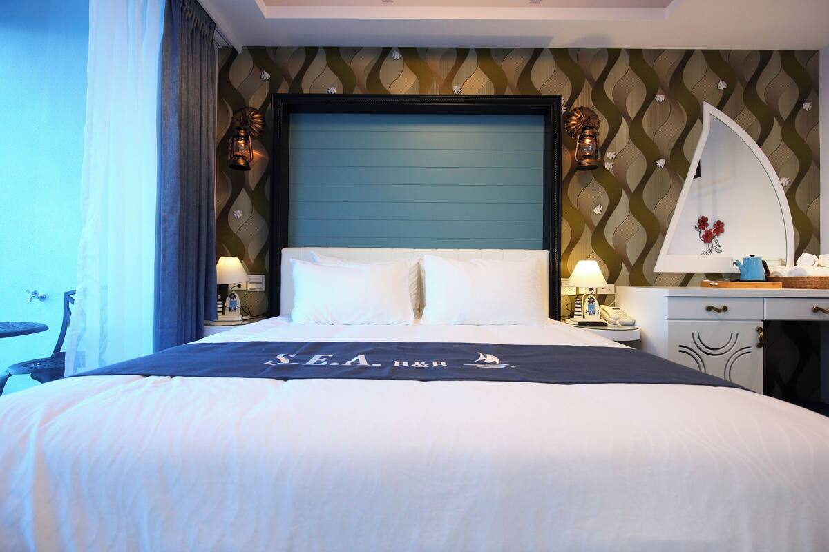 A hotel room with a large bed, a desk with a lamp, a mirror, and a wall with a patterned design.