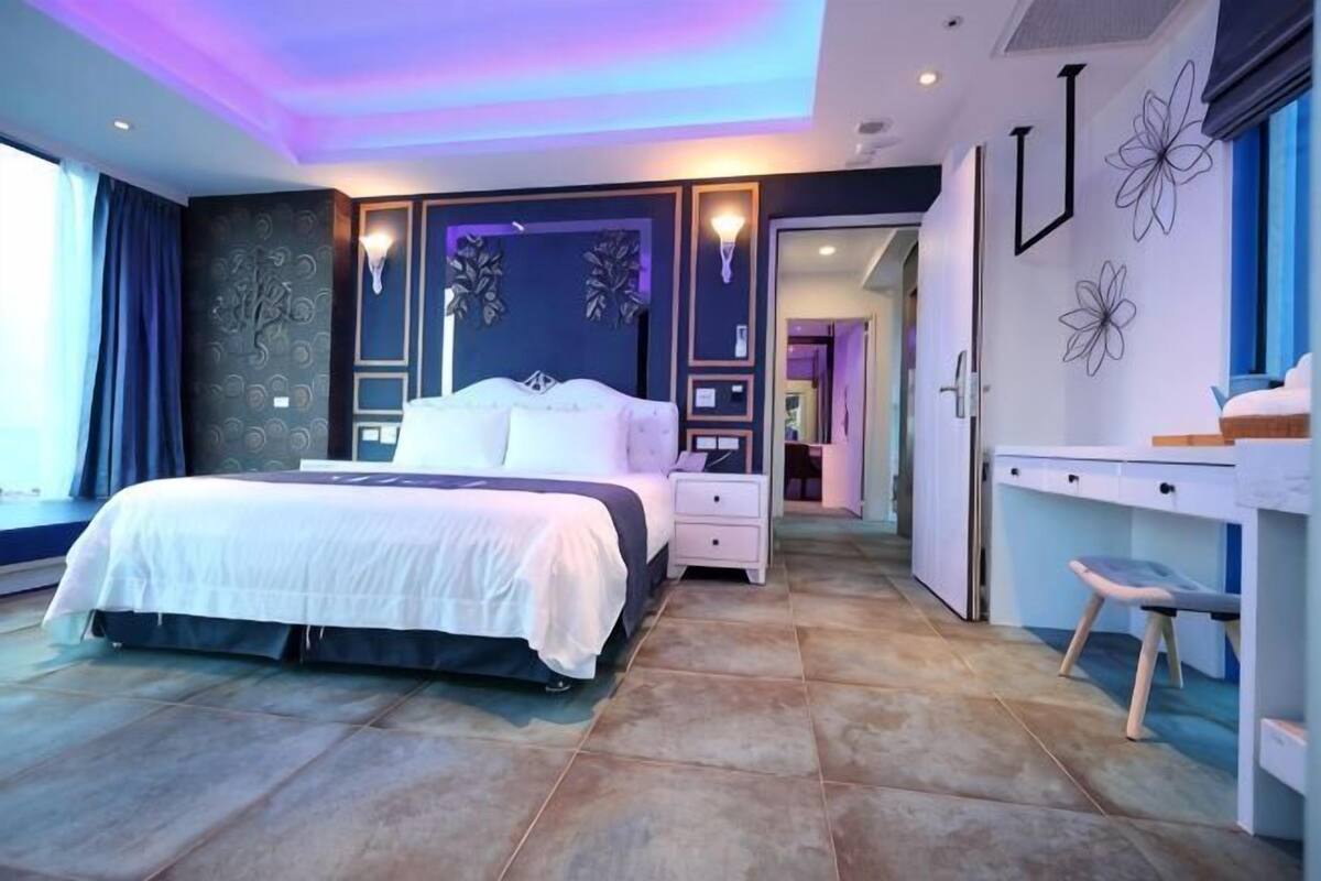 A modern bedroom with a large bed, bedside tables, a desk, and a chair.