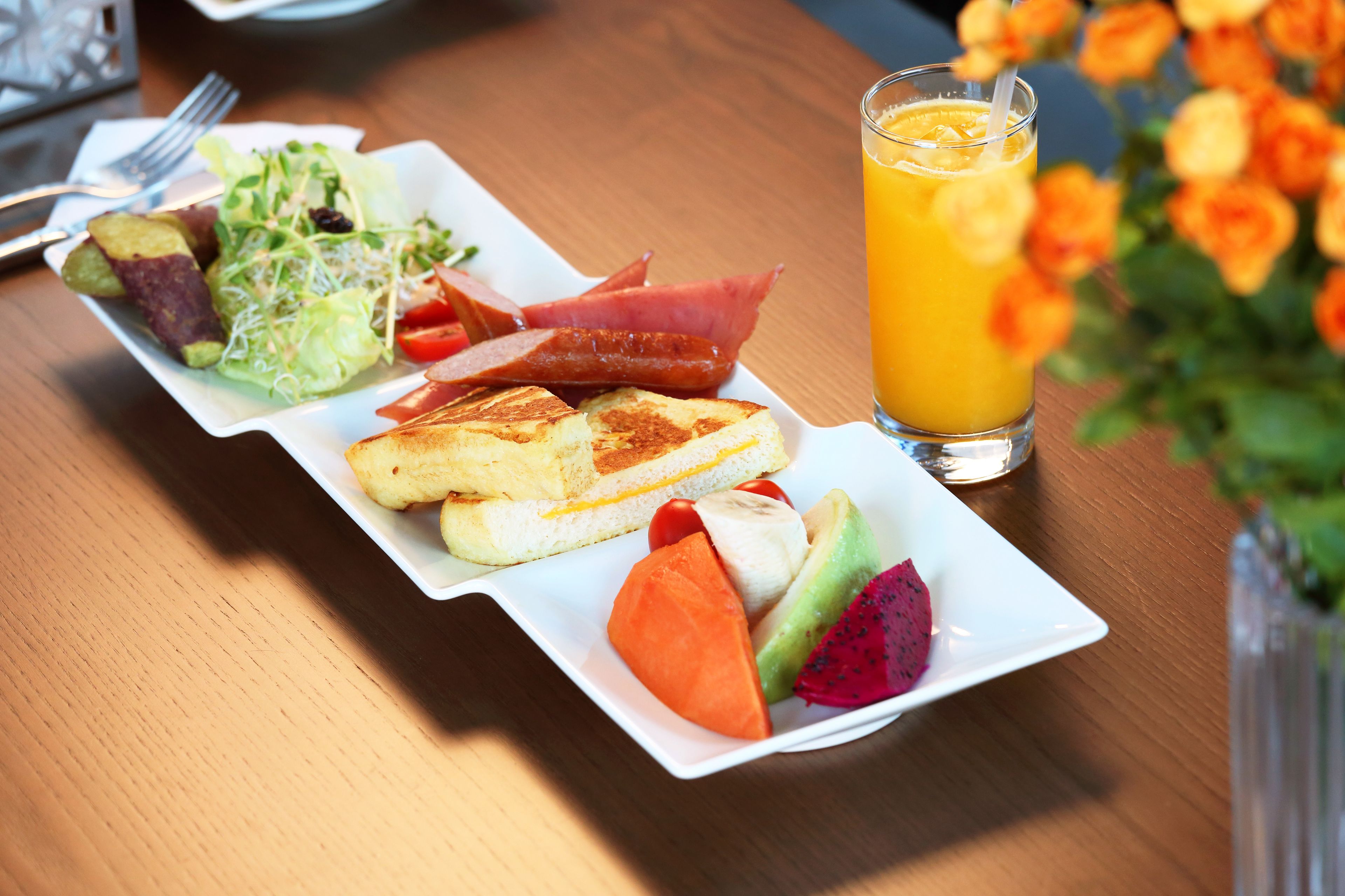 Un plato de desayuno con tostadas, fruta y un vaso de zumo de naranja sobre una mesa de madera.