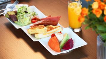 Un plato de desayuno con tostadas, fruta y un vaso de zumo de naranja sobre una mesa de madera.