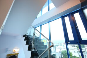 Un escalier moderne avec des rampes en verre et une vue sur la ville à travers de grandes fenêtres.
