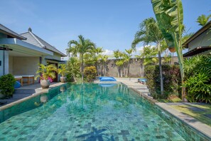 A clear swimming pool with tiled edges, surrounded by lush greenery and palm trees. - Villa Koru (Seminyak)