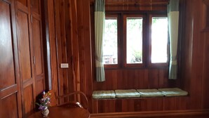 A wooden room with a bench, a table with a vase of flowers, and a window with curtains. - Chantara Resort (Bang Khonthi)