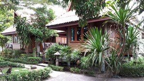 A wooden house with a porch, surrounded by lush greenery and a gravel path. - Chantara Resort (Bang Khonthi)