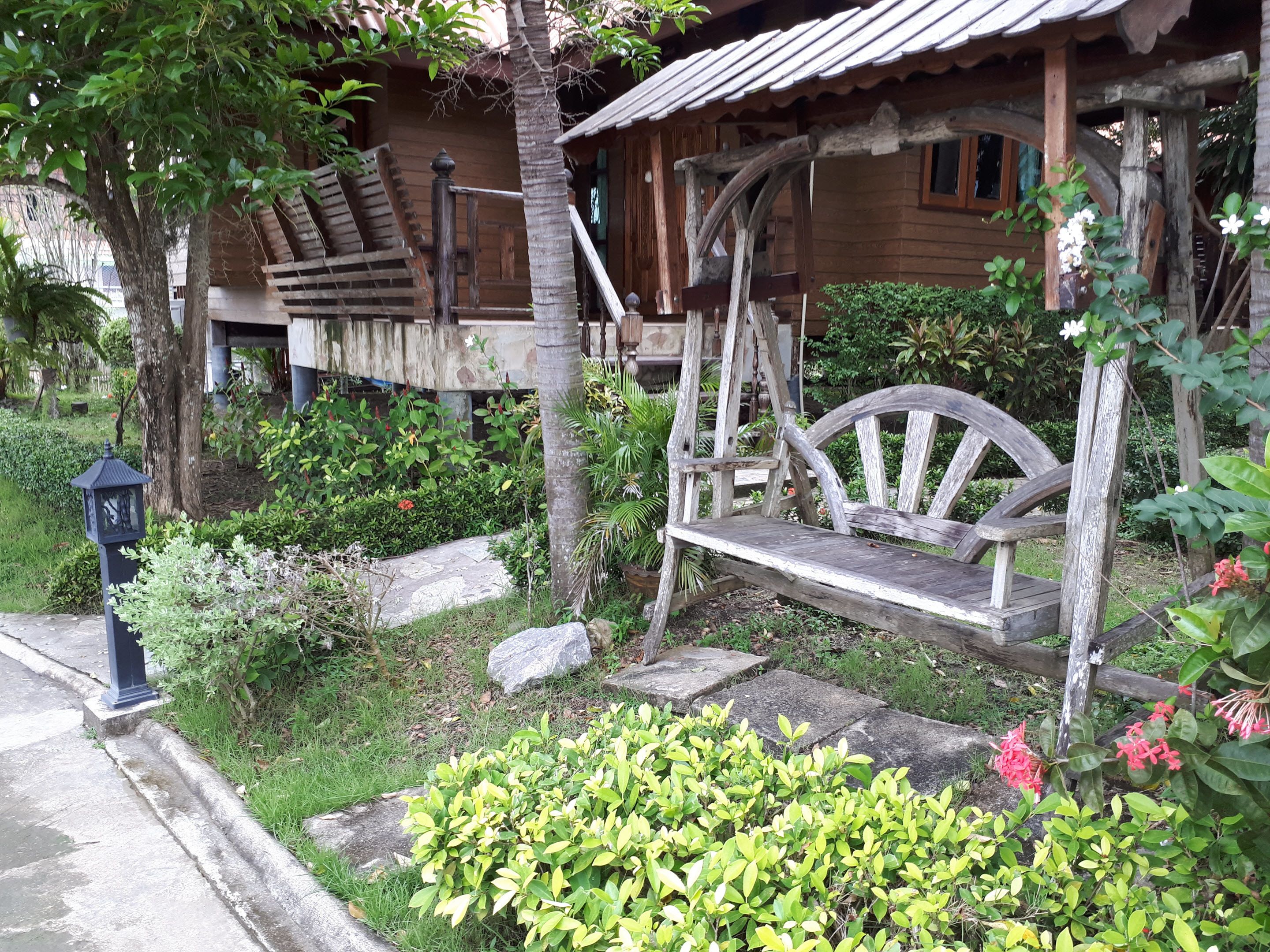 Una casa de madera rústica con un porche, una hamaca y un jardín lleno de plantas y flores.