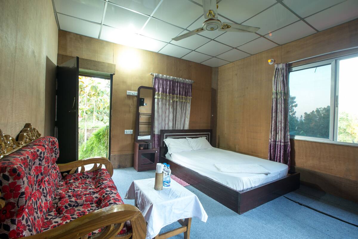 Una habitación con una cama, un sofá, una mesa con una botella y una taza, y una ventana con cortinas.