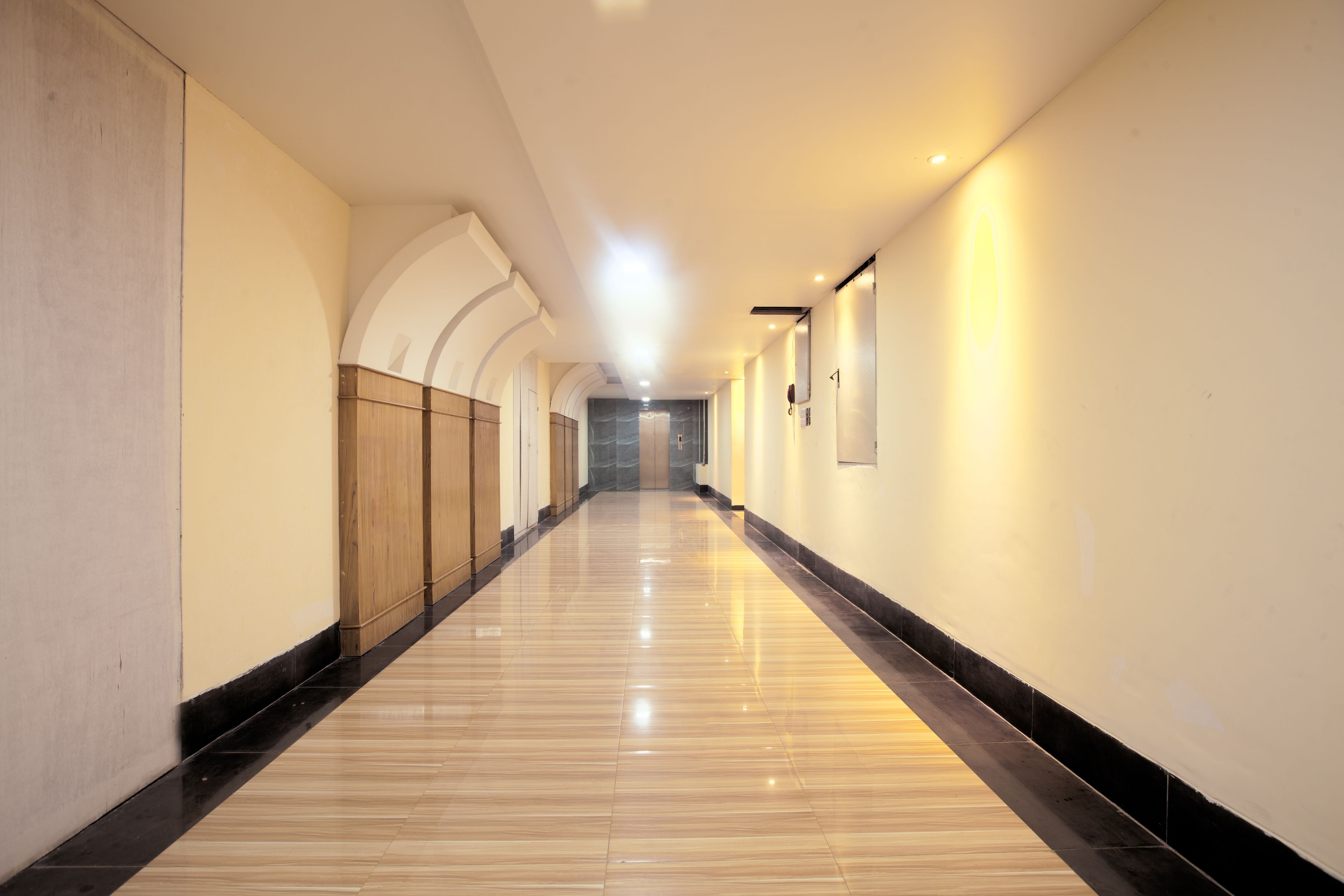 A long, well-lit hallway with a polished floor, wooden paneling on one side, and a plain wall on the other.