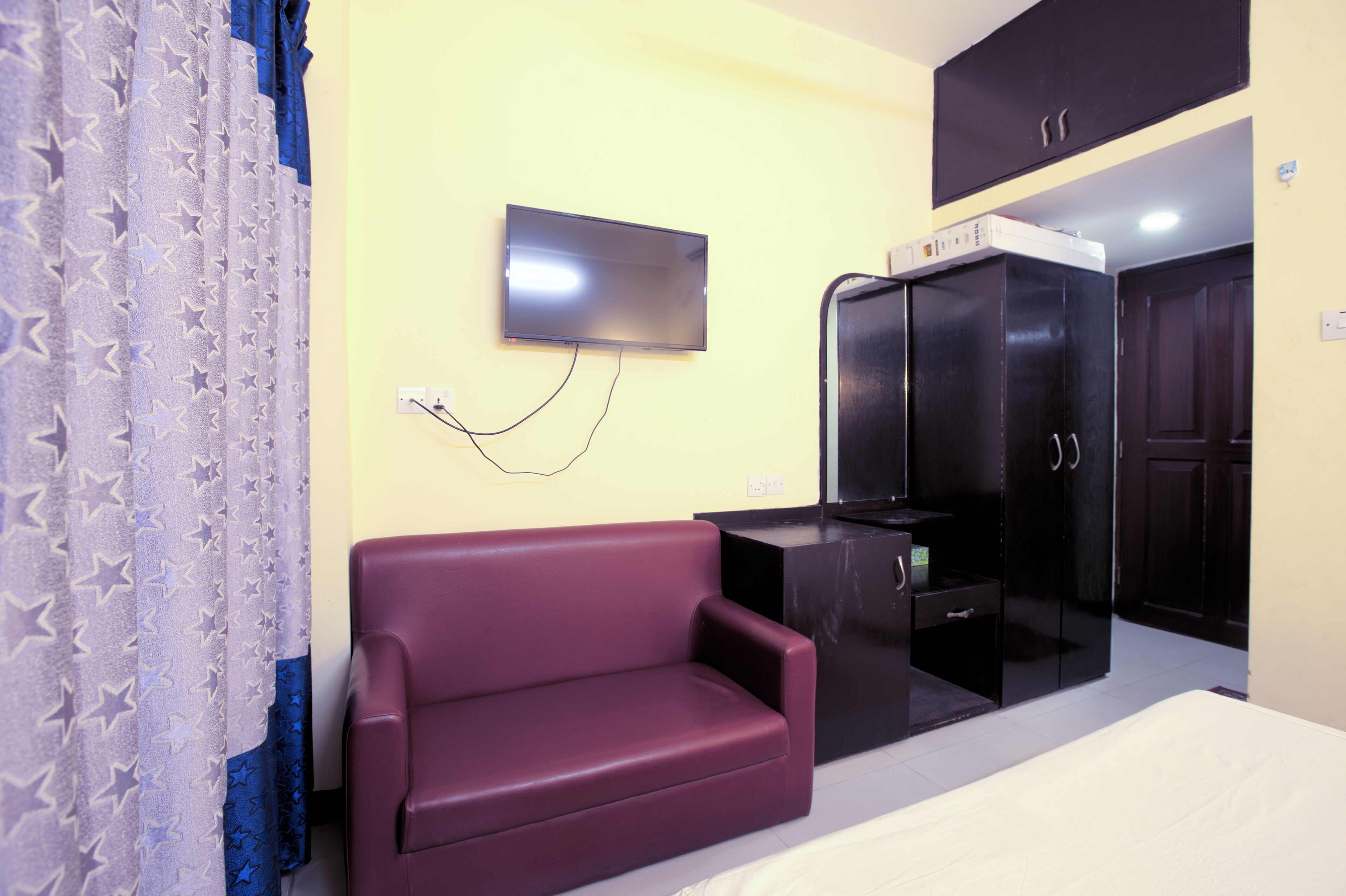 A bedroom with a bed, a TV mounted on the wall, a wardrobe, and a sofa.