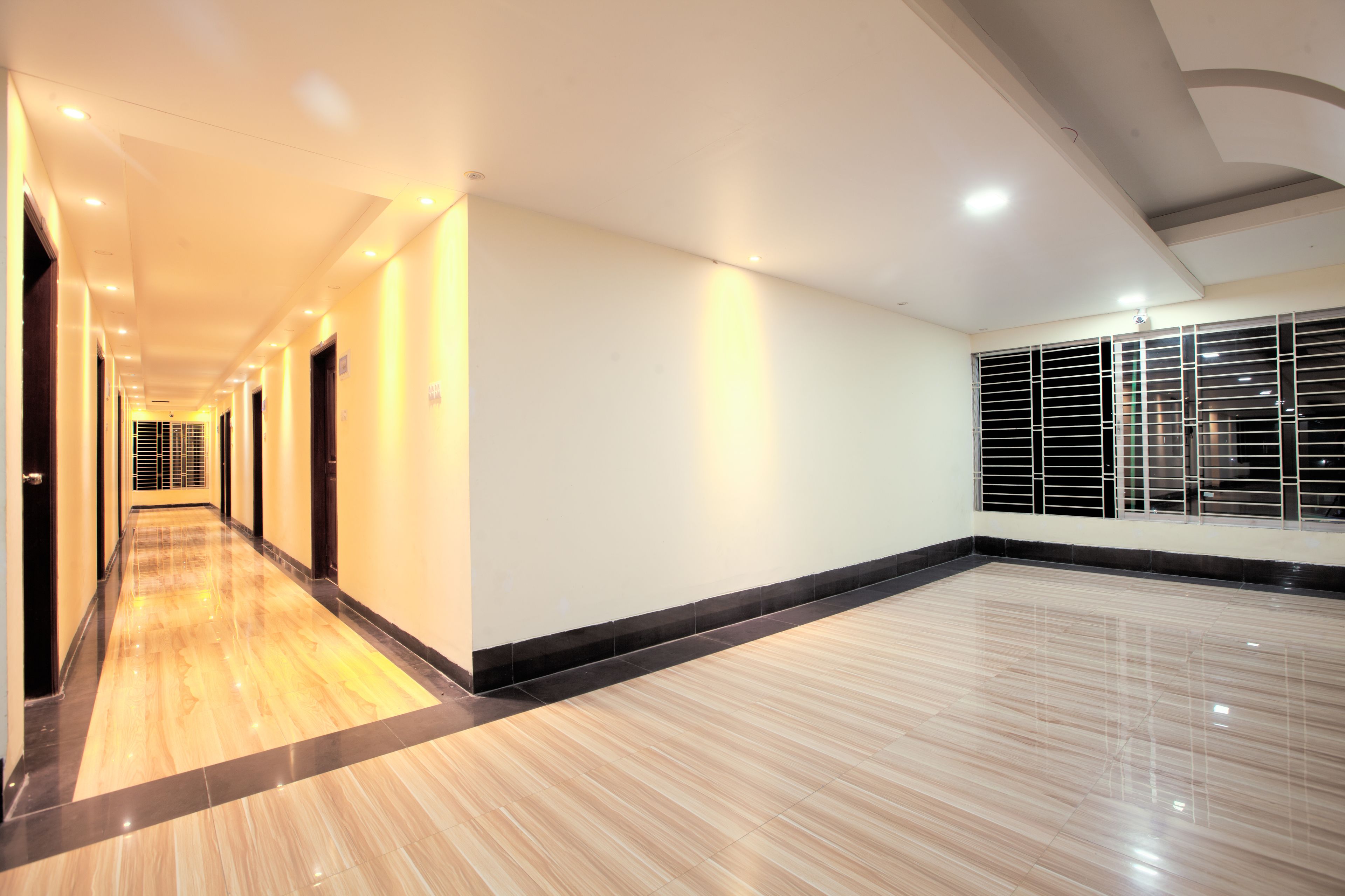 A hotel corridor with a polished wooden floor, white walls, and a series of doors along one side.