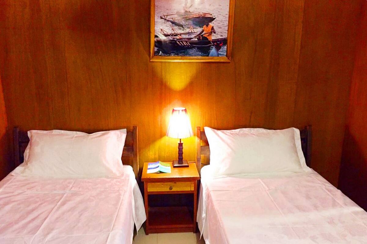 A room with two single beds, a nightstand with a lamp, and a painting on the wall.
