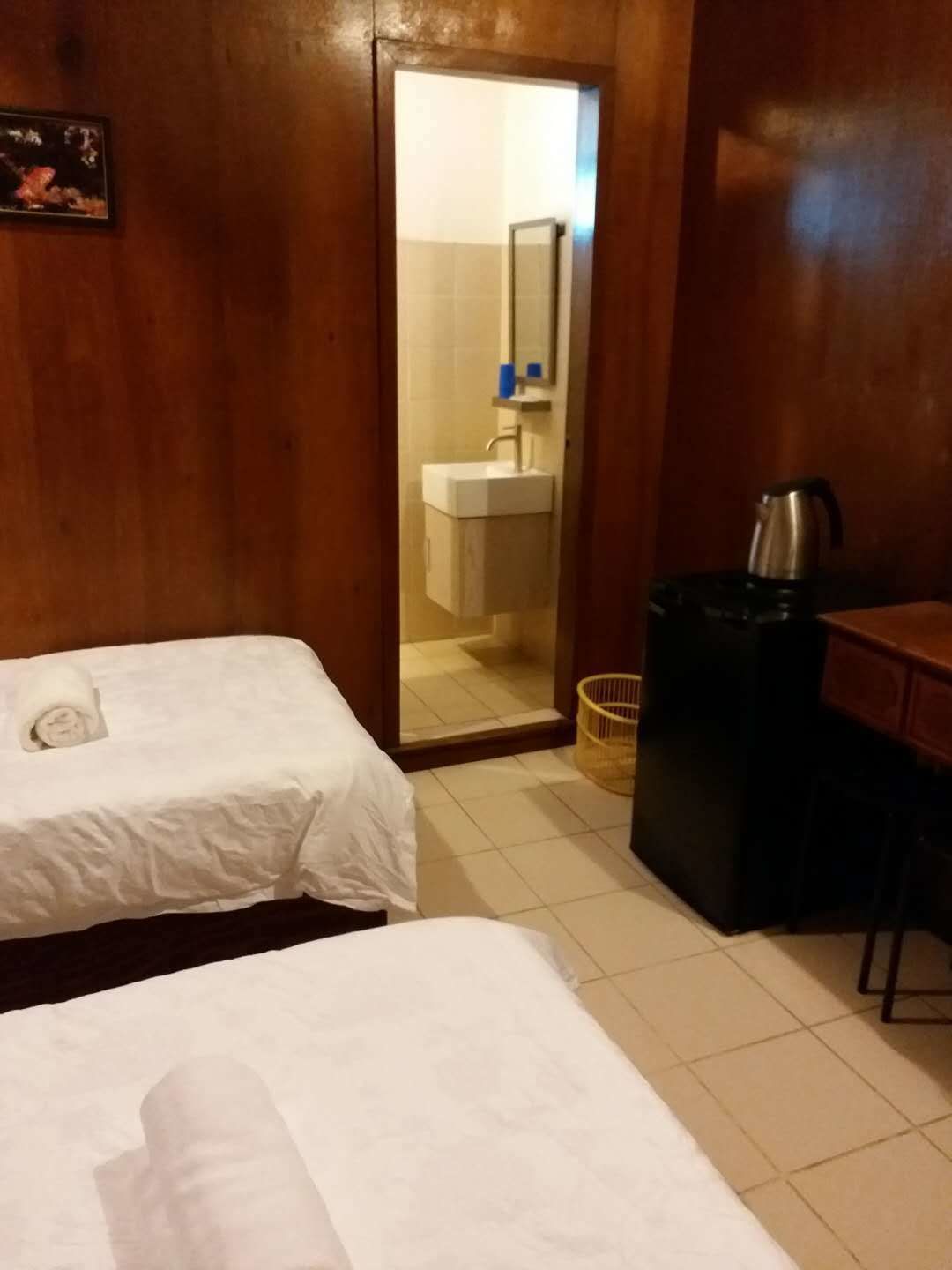Habitación de hotel con dos camas individuales, un escritorio de madera, una cafetera y un baño visible a través de una puerta abierta.