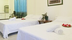 Une chambre d’hôtel avec deux lits, une petite table, une chaise, une plante en pot et un tableau encadré au mur.