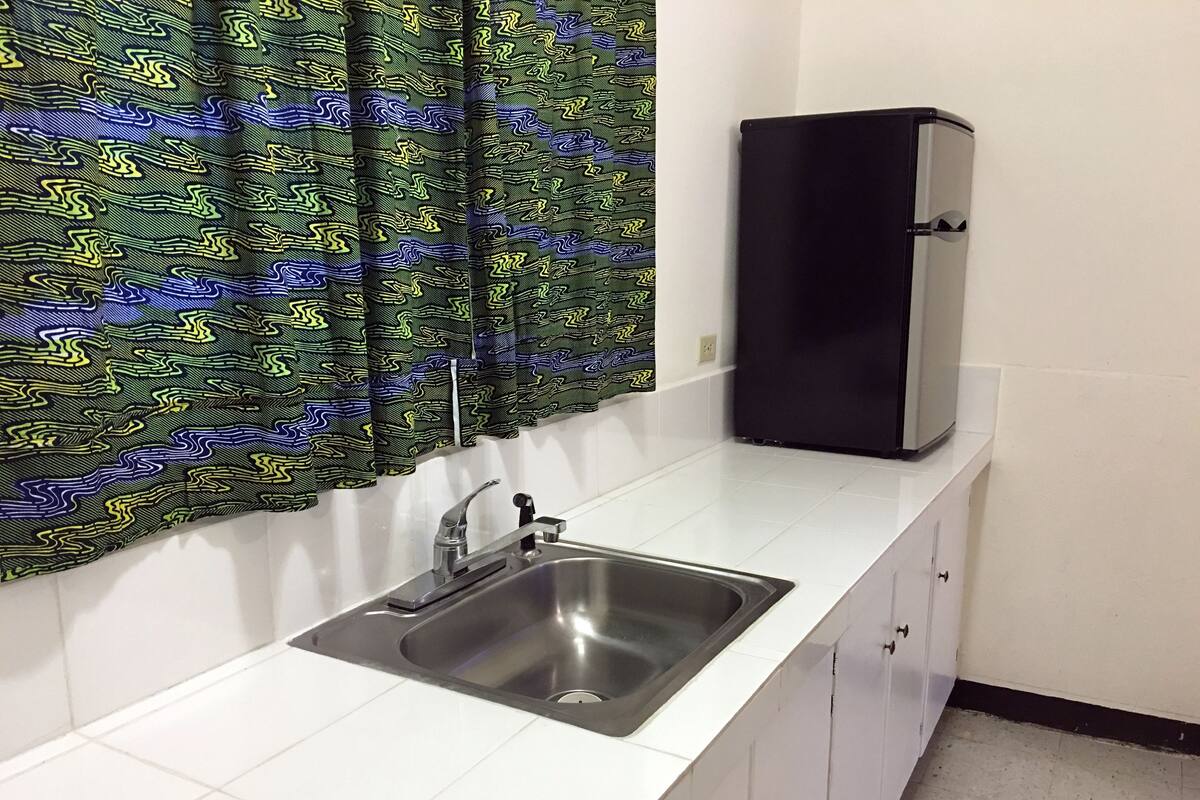 A kitchen with a stainless steel sink, white cabinets, and a black refrigerator.