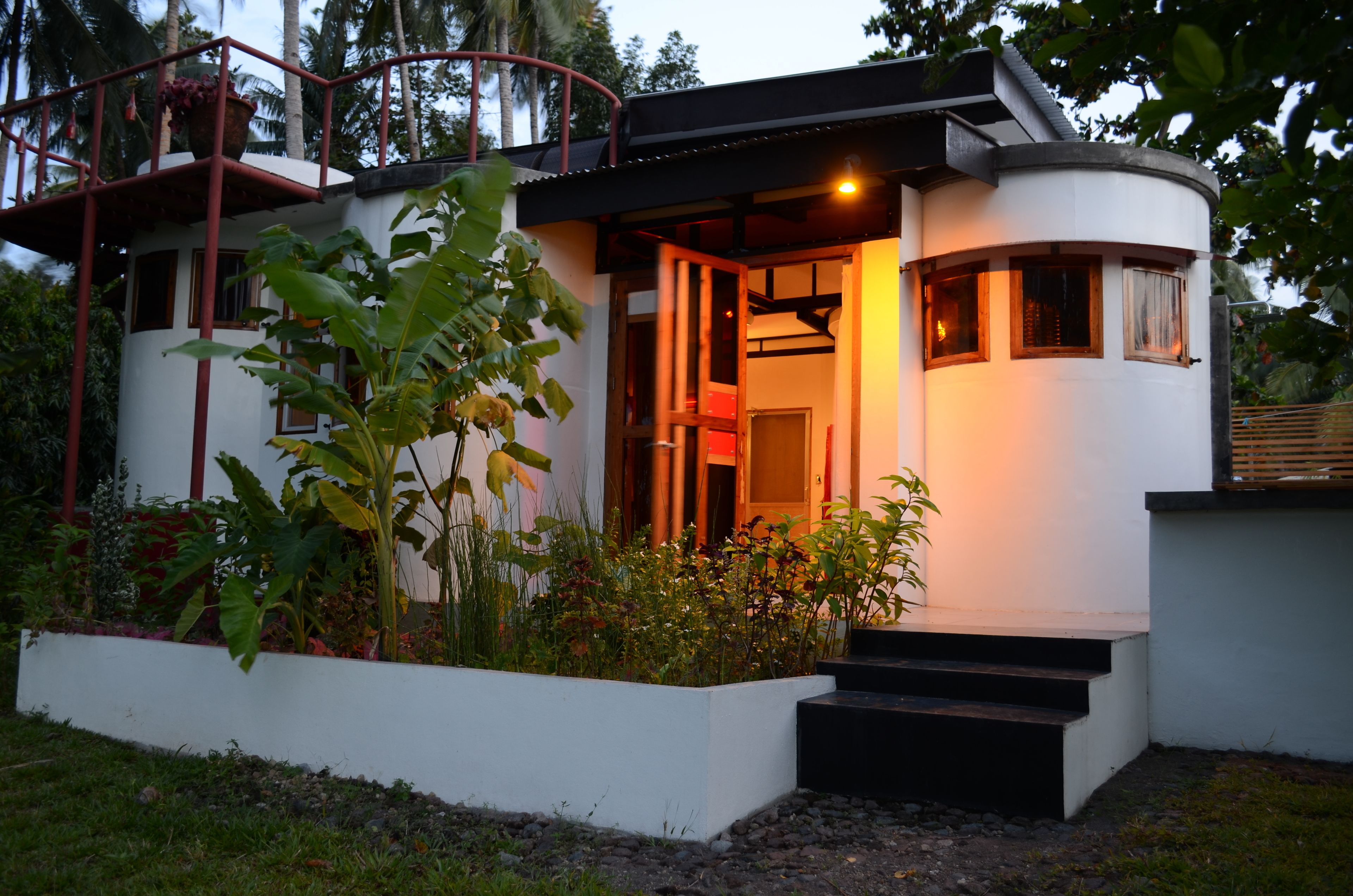 A modern house with a curved design, a balcony, and a well-maintained garden.