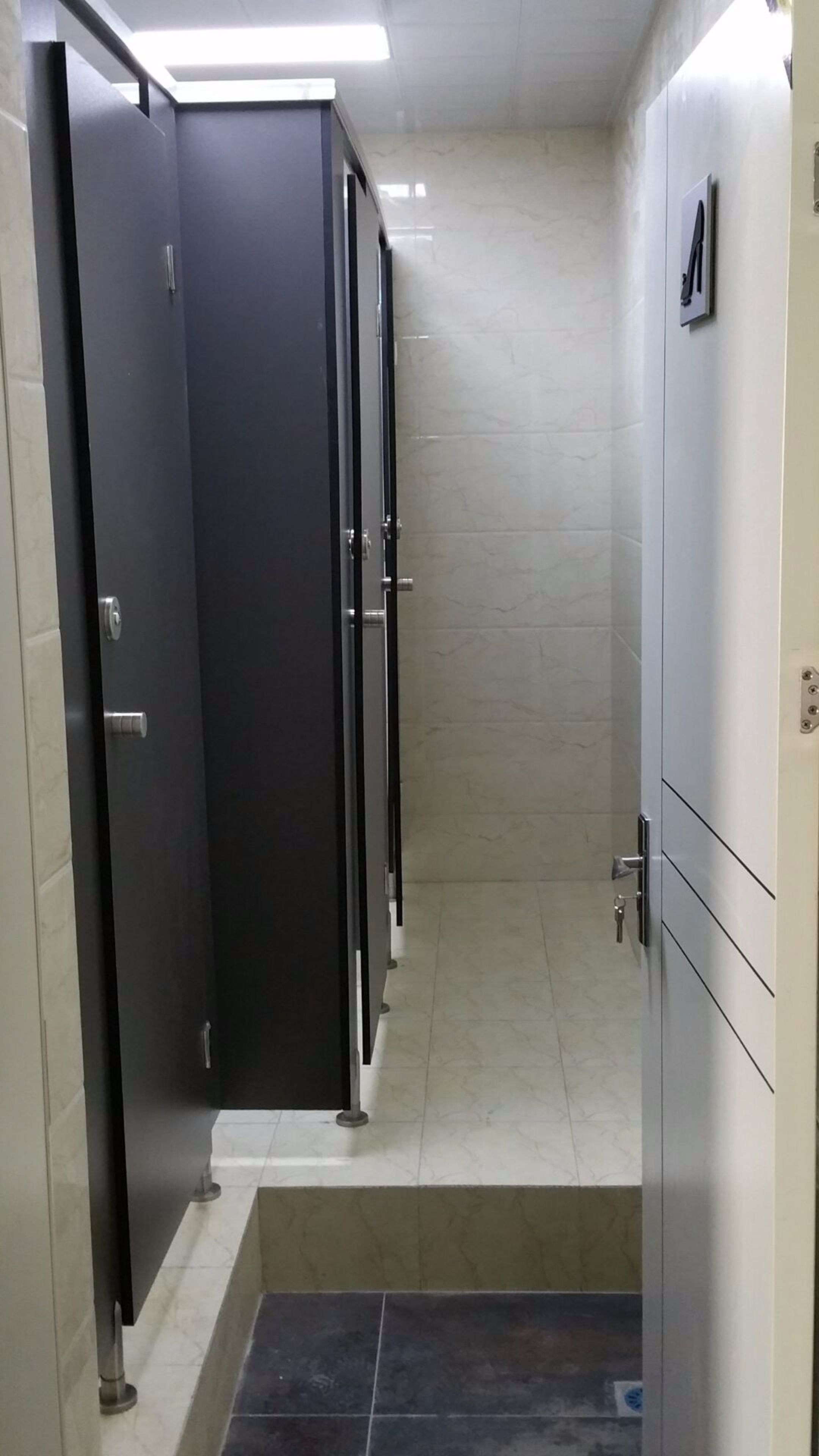 Eine Toilette mit mehreren Kabinen, gefliestem Boden und einer Metalltür.