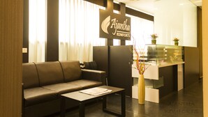 A reception area with a sofa, a coffee table, and a reception desk with a sign that reads "Ajantha Komforts." - Ajantha Komforts (Bengaluru)