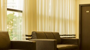 A room with a sofa and a chair near a window with sheer curtains, a door with a number, and a striped curtain. - Ajantha Komforts (Bengaluru)