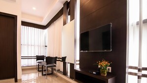 A modern hotel room with a large flat-screen TV mounted on the wall, a seating area with two chairs, and a decorative plant on a console table. - Ajantha Komforts (Bengaluru)