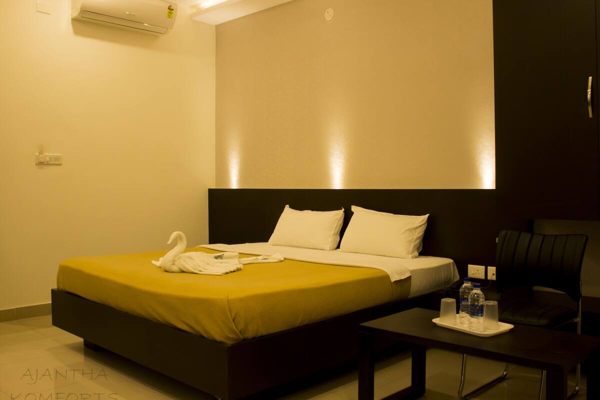A modern hotel room with a large bed, a bedside table with a tray, and a chair.