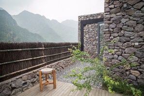 A wooden deck with a stone wall and a bamboo fence overlooking a mountainous landscape.