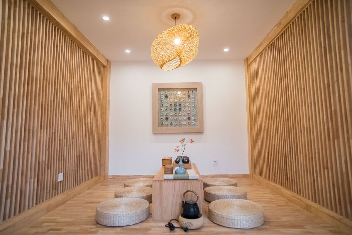 A room with a wooden slat wall, a hanging light fixture, a framed artwork, a small wooden table with decorative items, and round seating.