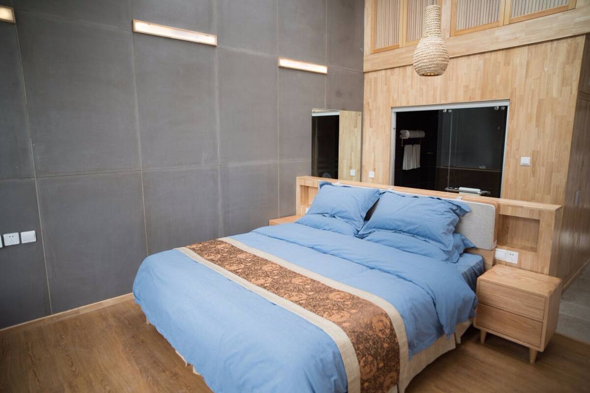 A modern bedroom with a large bed, wooden headboard, bedside tables, and a built-in wardrobe.
