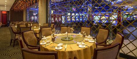 A dining area with a round table set for six, surrounded by chairs, and a view of slot machines in the background.