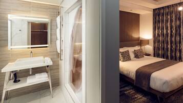 A modern hotel room with a large bed, a bedside table, a mirror, and a bathroom with a sink and towel rack.