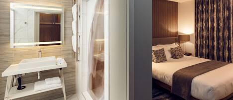 A modern hotel room with a large bed, a bedside table, a mirror, and a bathroom with a sink and towel rack.